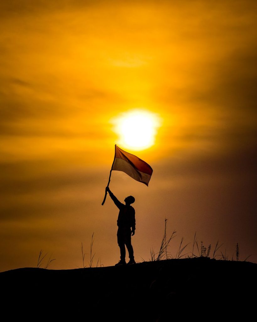 silhouette holding indonesian flag at sunset