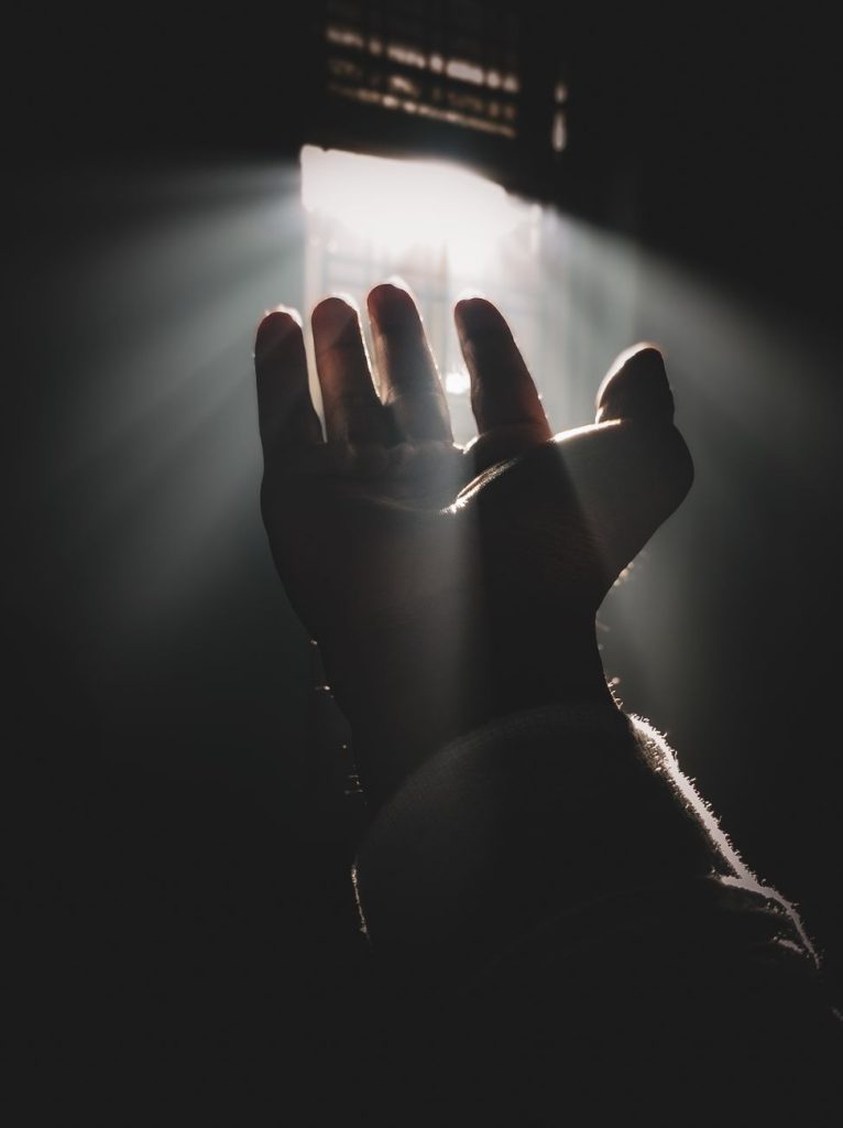 silhouette of a hand reaching for sunlight through window